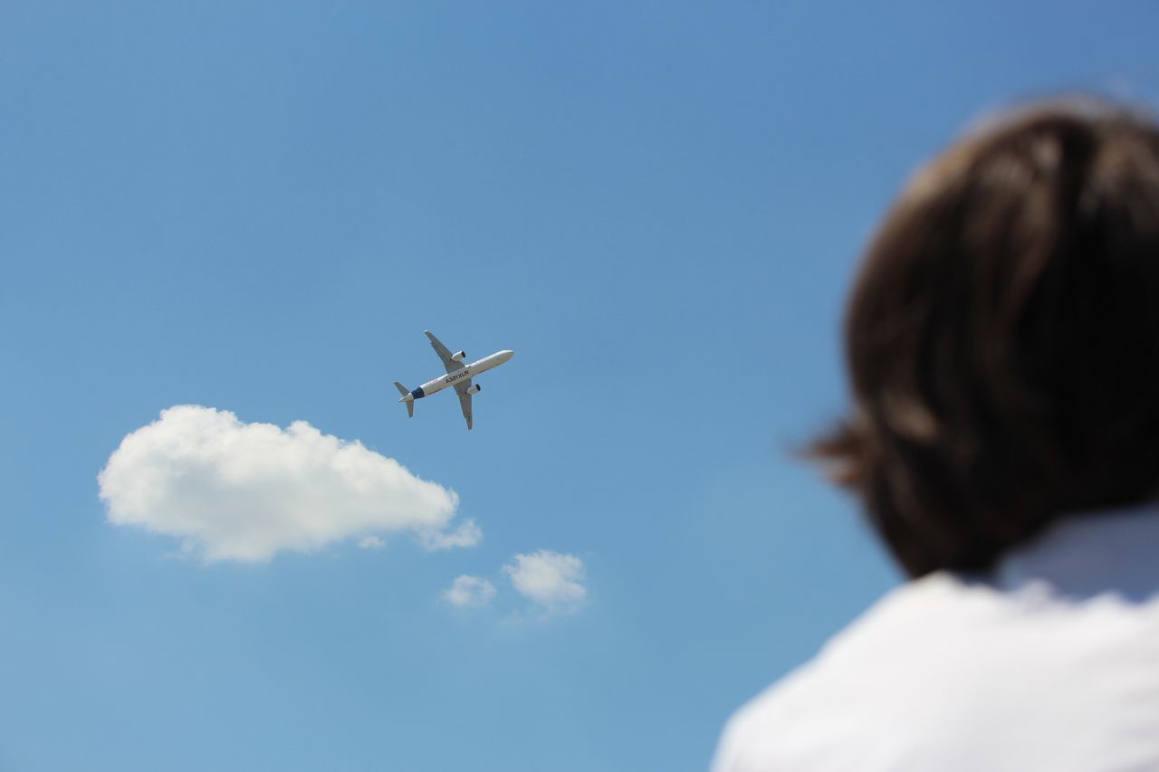 An airplane flies high in a clear sky while a person watches from below.
